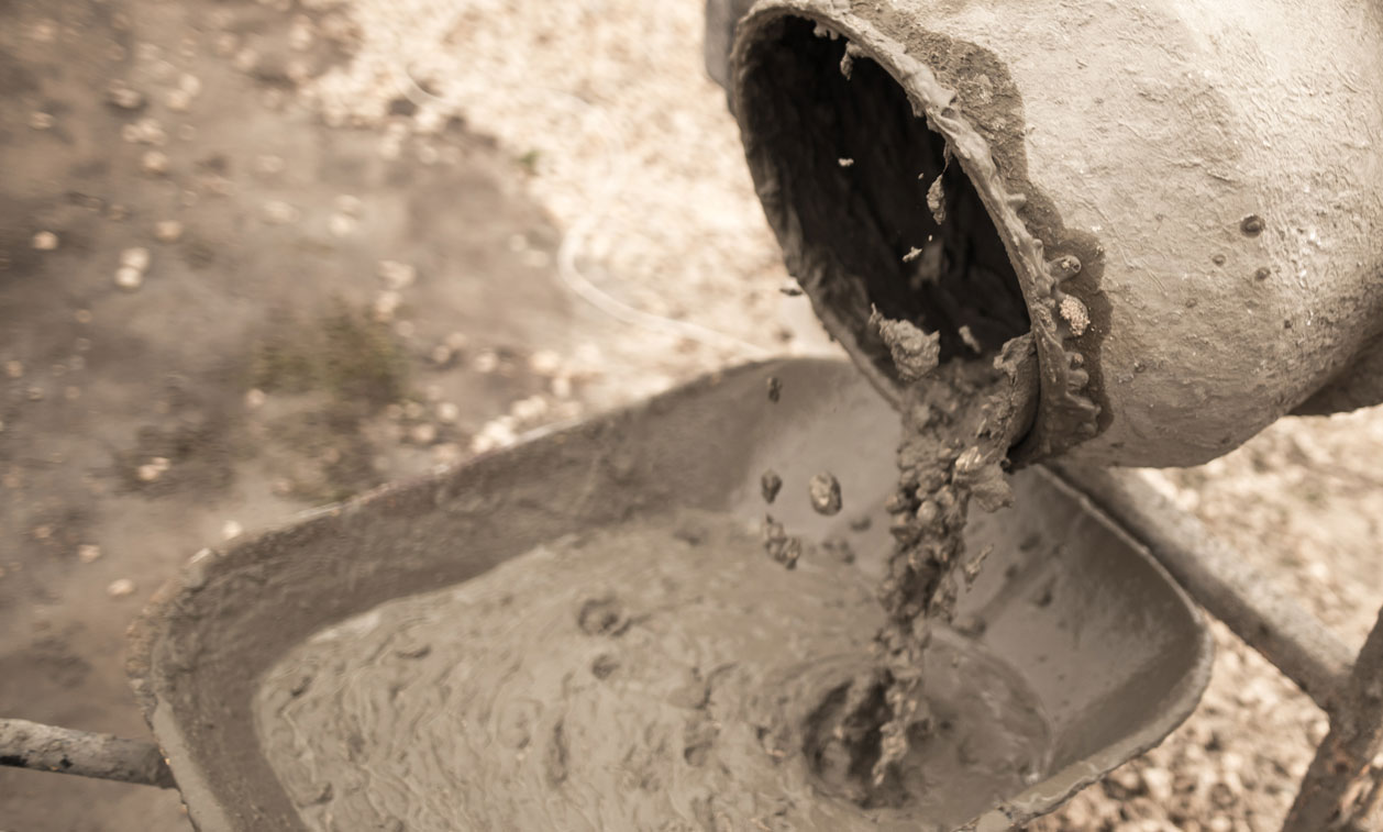 A close up of the side of a pipe with cement pouring out.